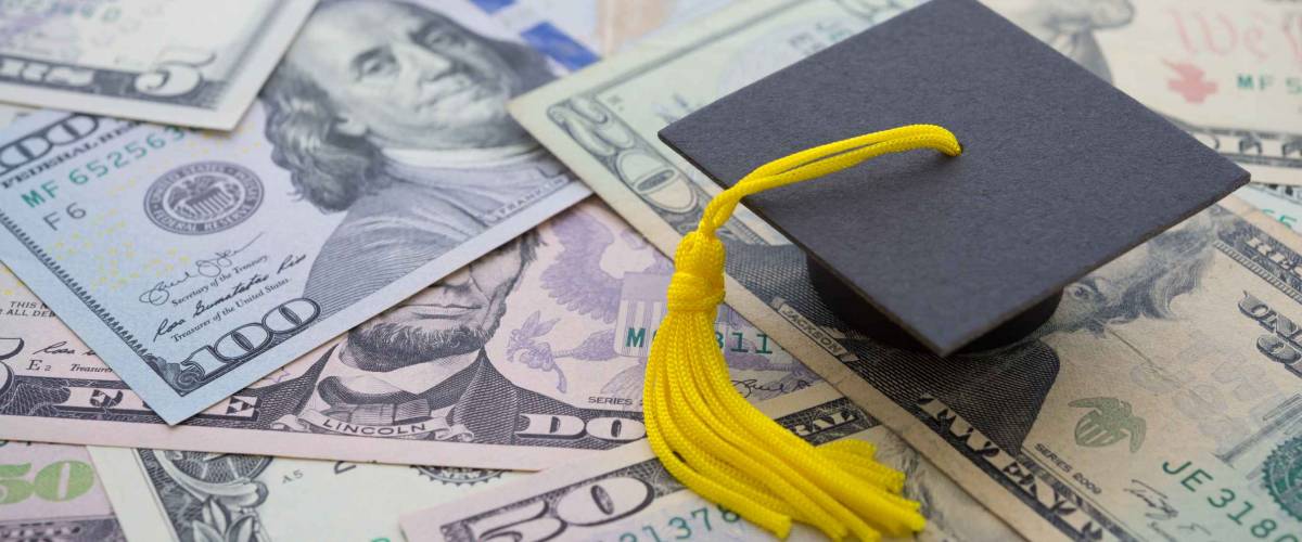 Graduation cap university or college degree on US dollars banknotes, representing student loan refinancing.