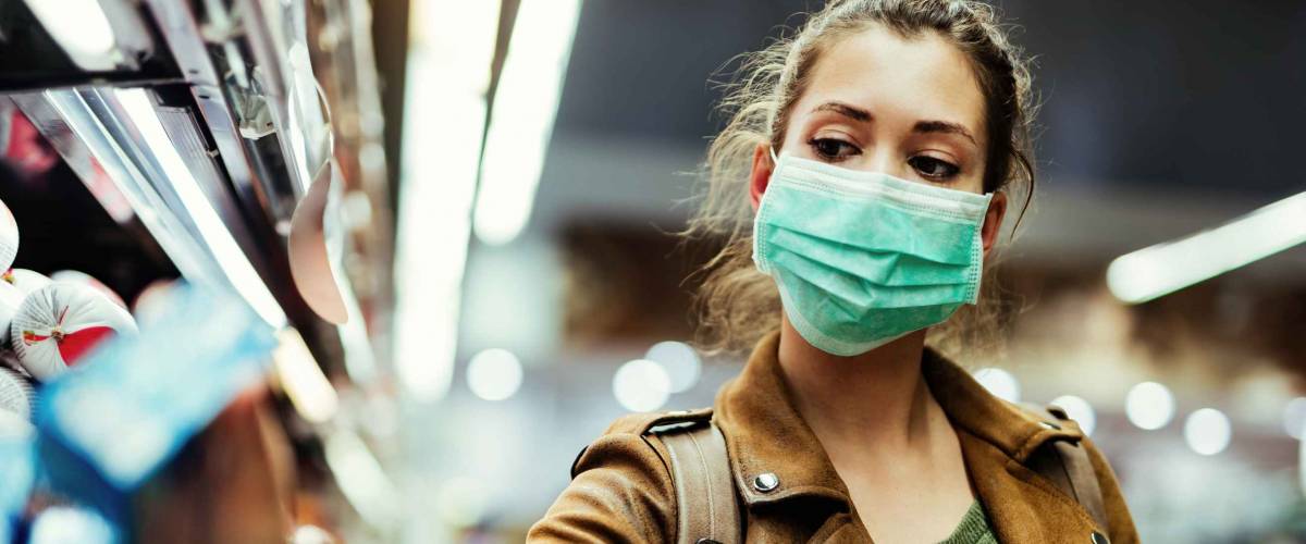 Young woman with face mask using mobile phone and buying groceries in the supermarket during virus pandemic.