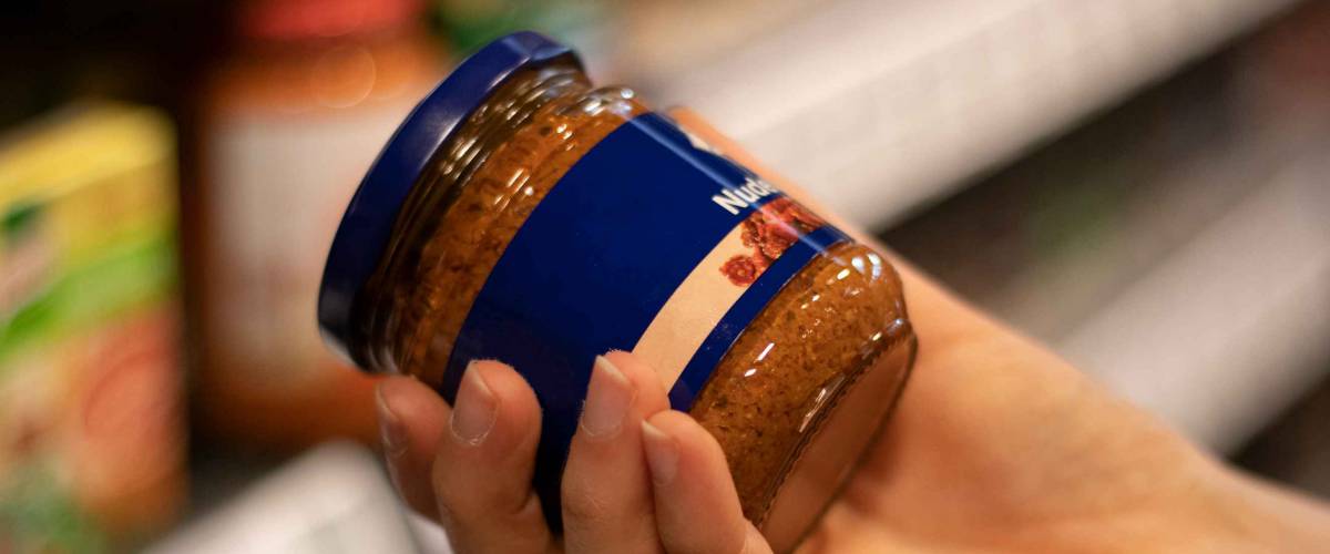 A woman holds a jar of pasta sauce in a supermarket.