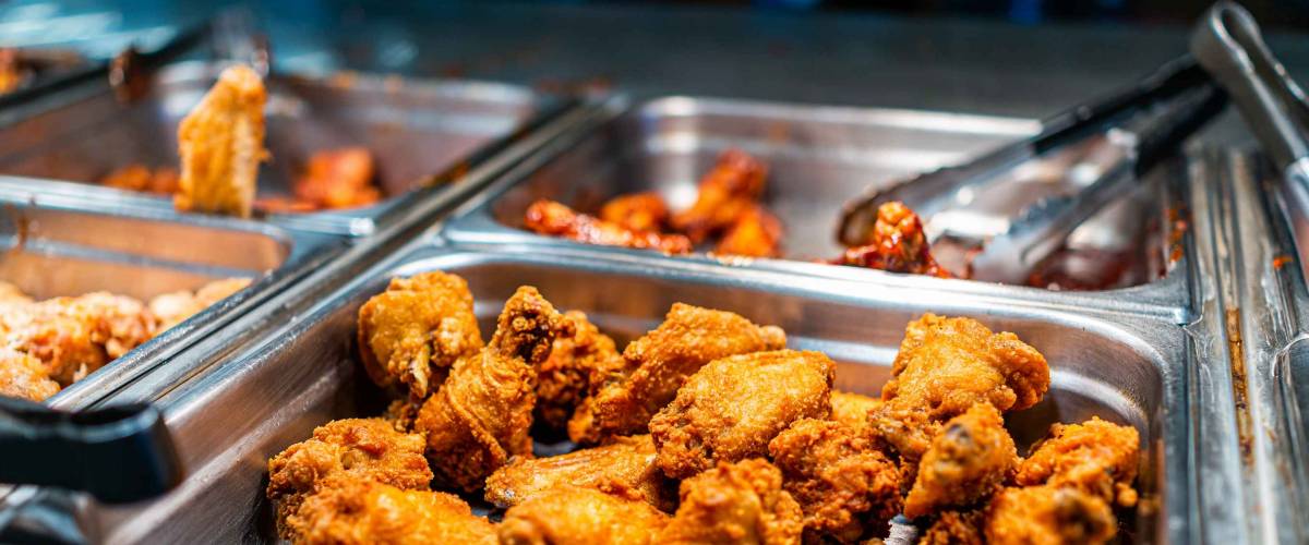Fried chicken thighs buffet bar self serve with tongs in grocery store, restaurant or catering event with crisp skin and unhealthy food