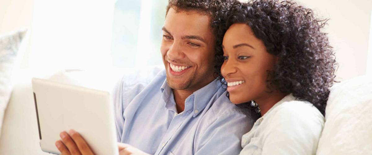 Young Couple Sitting On Sofa Using Digital Tablet
