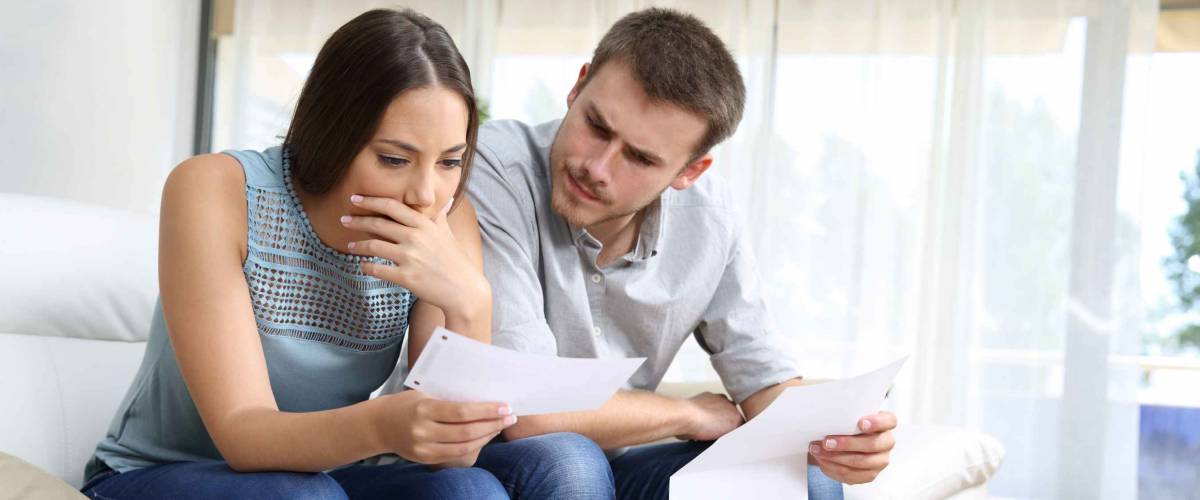 Worried couple checking receipt sitting in the sofa in the living room at home