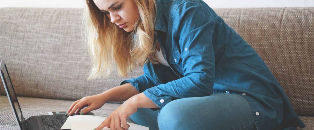 Serious woman focused on finding information on paper. Sitting at home in front of a laptop. The concept of business and online student learning