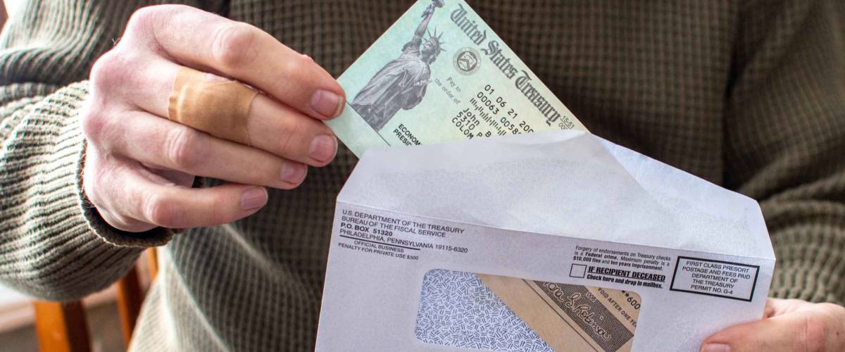 A man's hand holds a letter with a covid aid check from the USA government