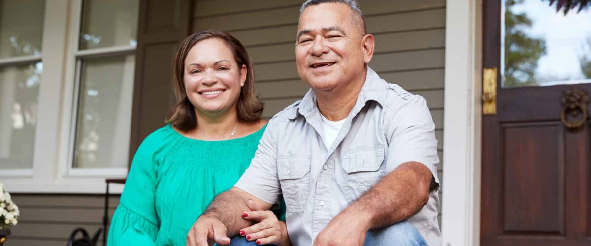 Portrait Of Smiling Senior Couple Sitting In Front Of Their Home