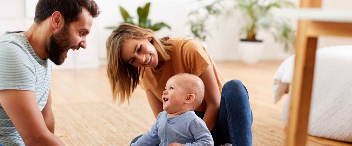 Parents Sitting On Floor At Home Playing With Baby Son