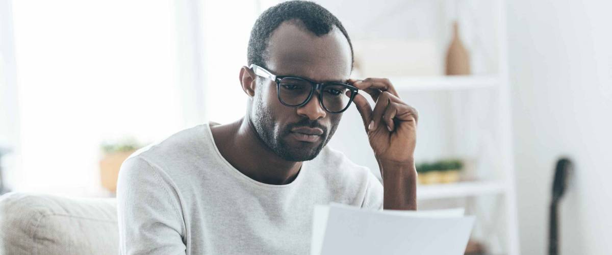 Man looking at piece of paper while holding glasses and sitting on the couch
