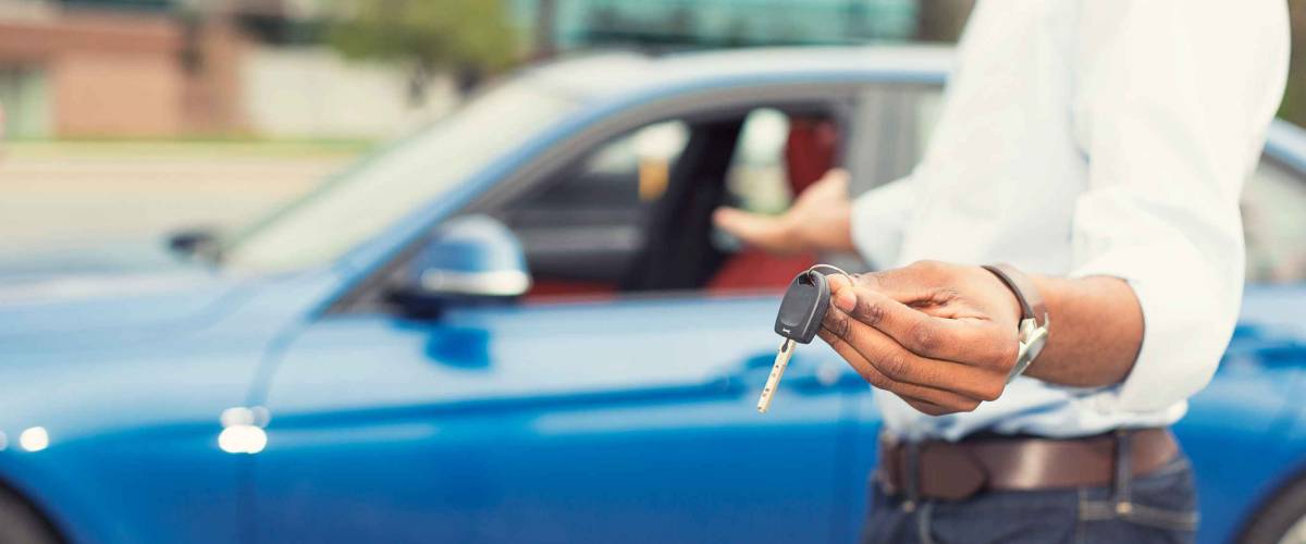 Male hand holding car keys offering new blue car in the background