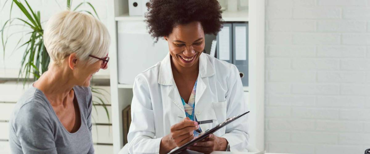 A female doctor sits at her desk and chats to an elderly female patient while looking at her test results