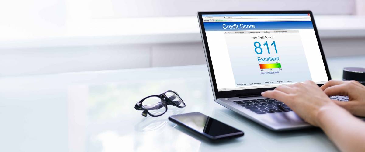 Person using laptop to check their credit score with phone and glasses placed beside the computer.