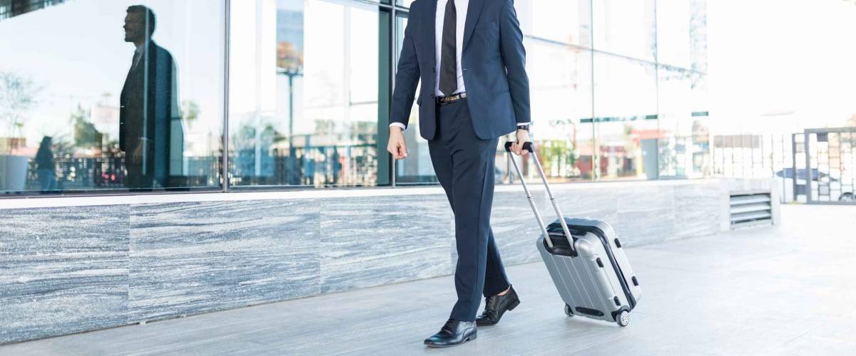Smiling and good looking manager with suitcase walking outside modern office