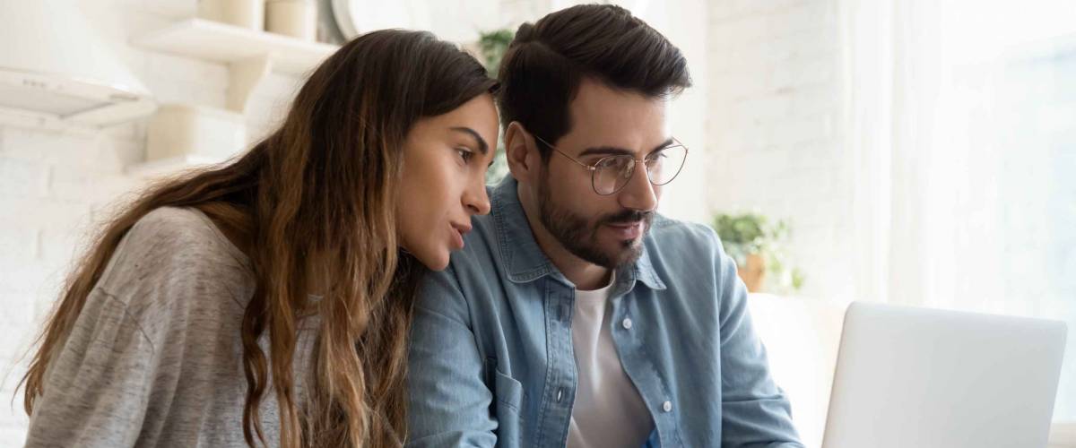Focused young couple looking at laptop screen together, figuring out finances.