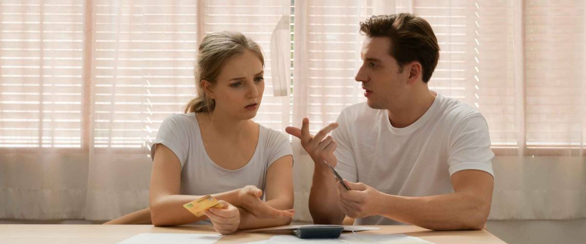 Couple sitting at table, arguing over finances.