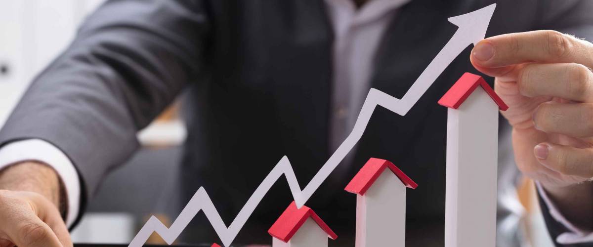 Businessman Holding Paper Graph Over The Increasing House Miniature