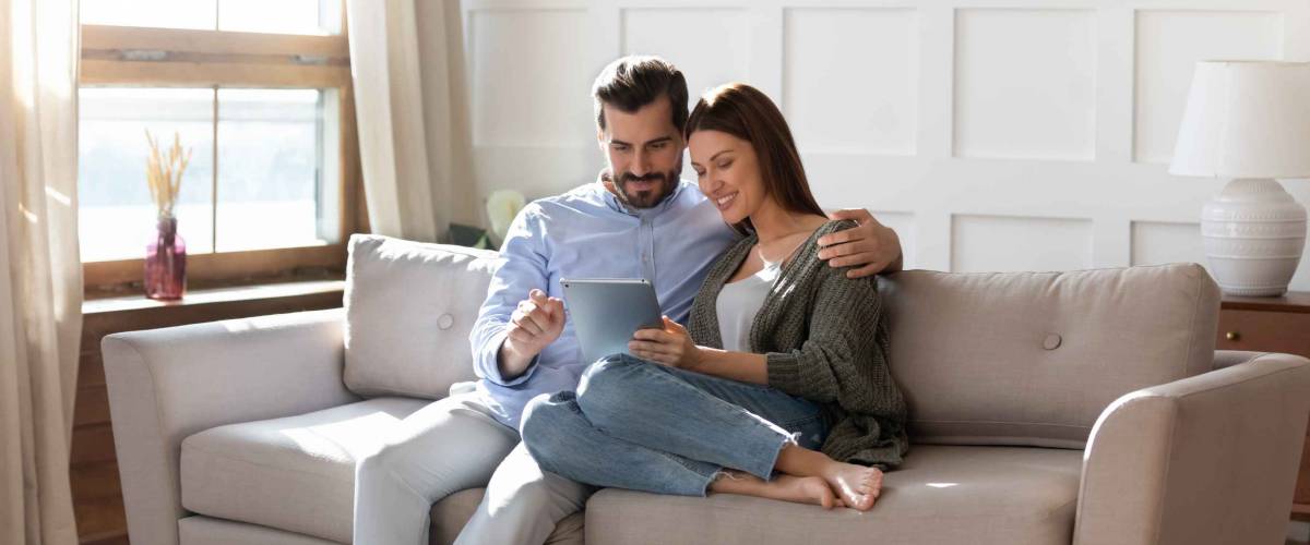 Happy looking couple sitting closely on couch, looking at tablet together