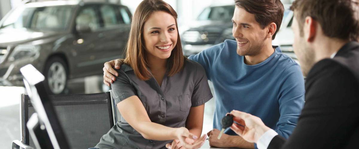Now her dream comes true. Car salesman giving the key of the new car to the young attractive owners