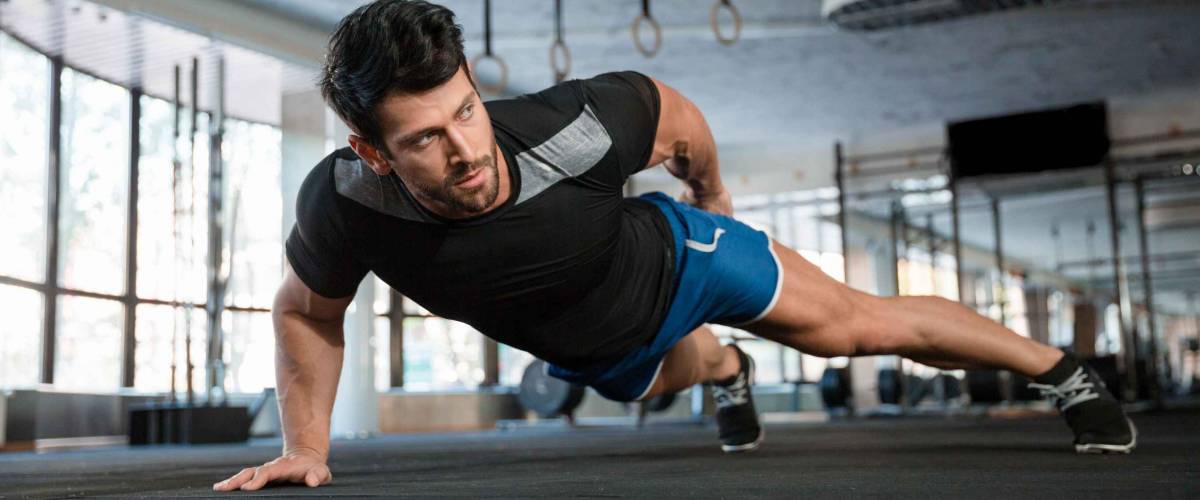 Portrait of a handsome man doing push ups exercise with one hand in fitness gym