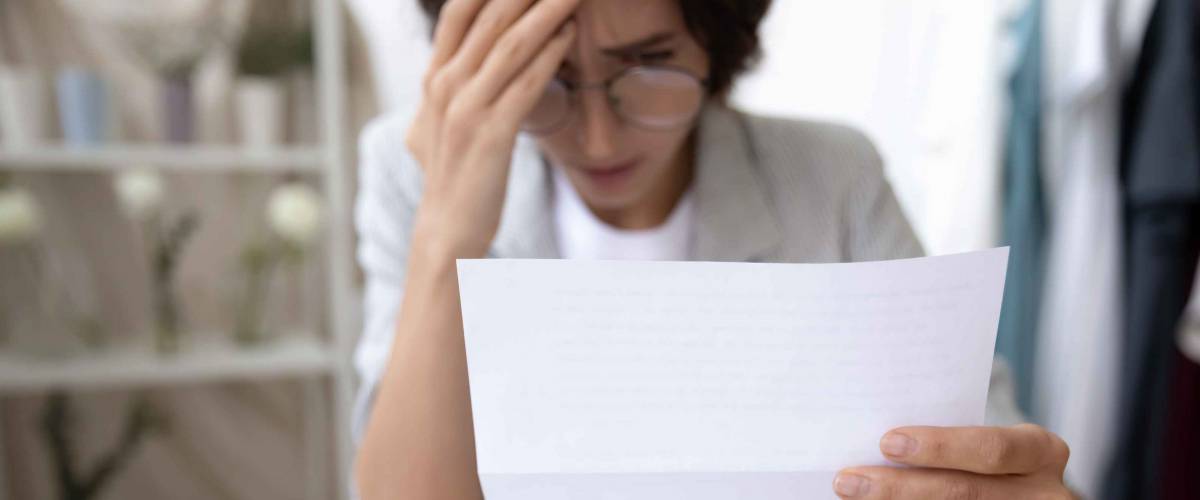 Upset woman looking at a piece of paper, holding head in her hand.