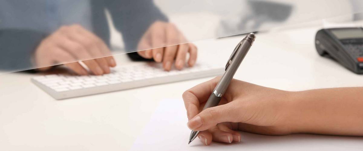 Woman signing piece of paper in front of bank teller, close up of hands