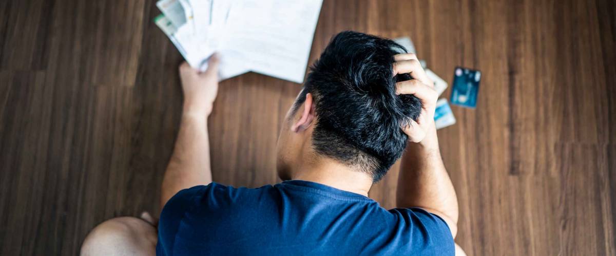 Top view of stressed young Asian man putting hands on head trying to find money to pay credit card debt