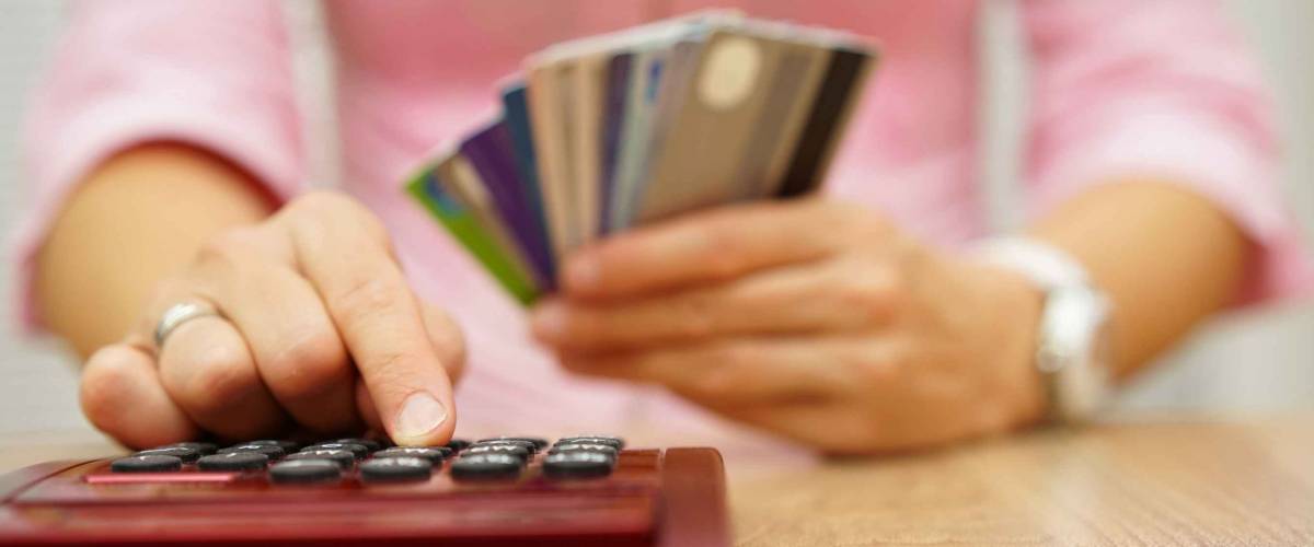 Close up of woman holding a stack of credit cards, punching numbers into a calculator.