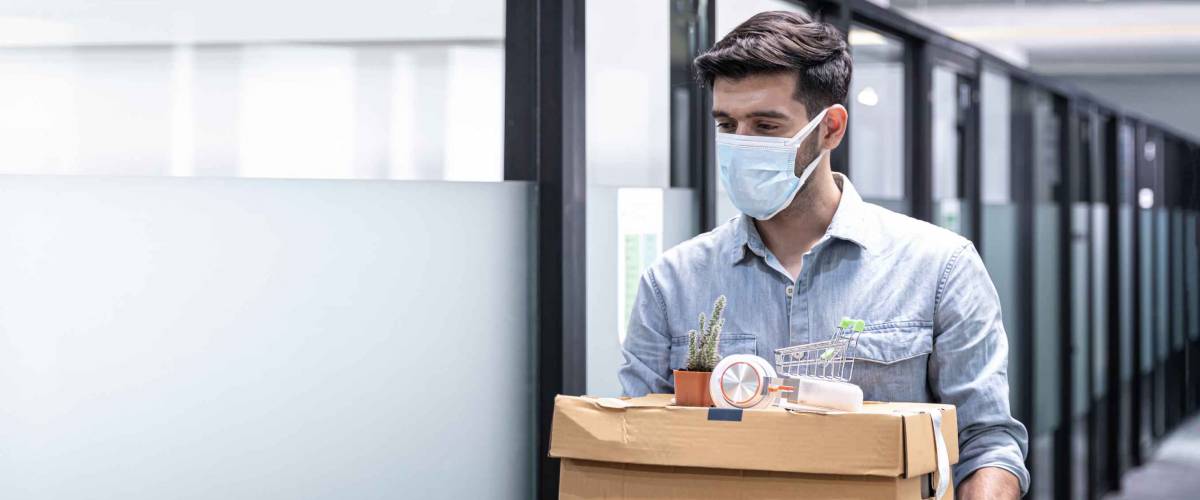 Man carrying box of things out of office, wearing a face mask.