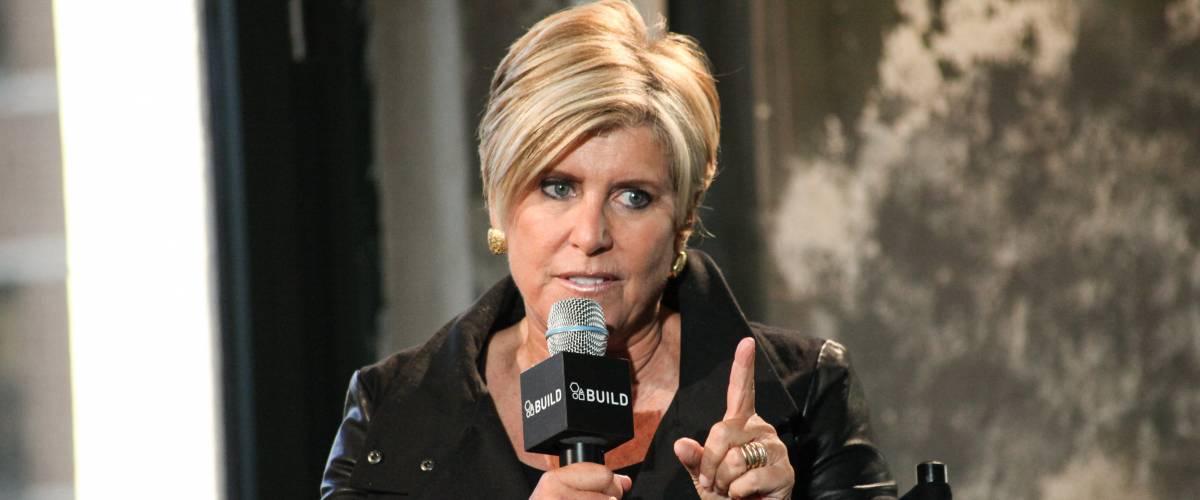 Suze Orman holding a microphone and pointing her finger while talking.