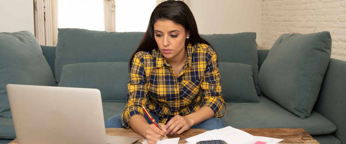 Young worried woman in stress banking and accounting debt bills, bank papers, expenses and payments with computer at home feeling desperate in a bad financial situation.