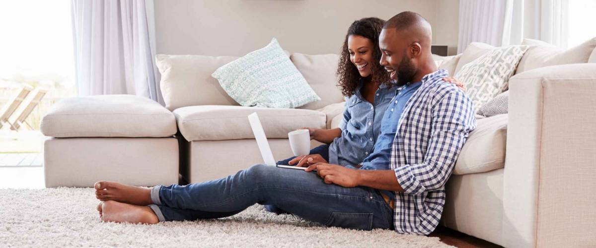 Young black couple sit on the floor using laptop, side view