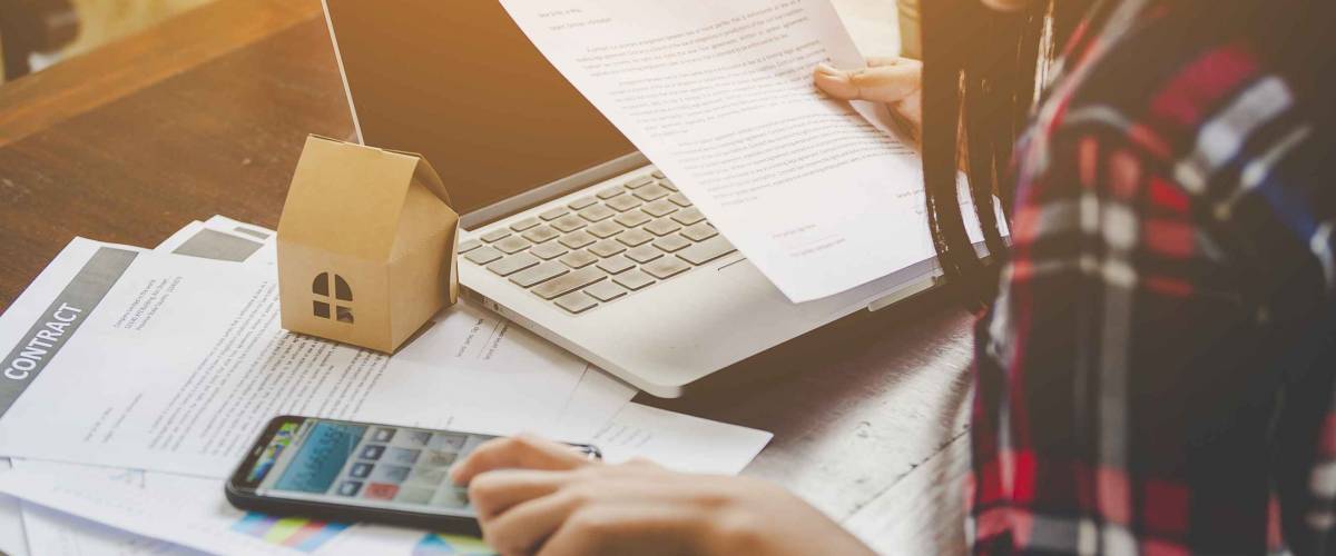 Woman looking at insurance documents and using a calculator to add up numbers.