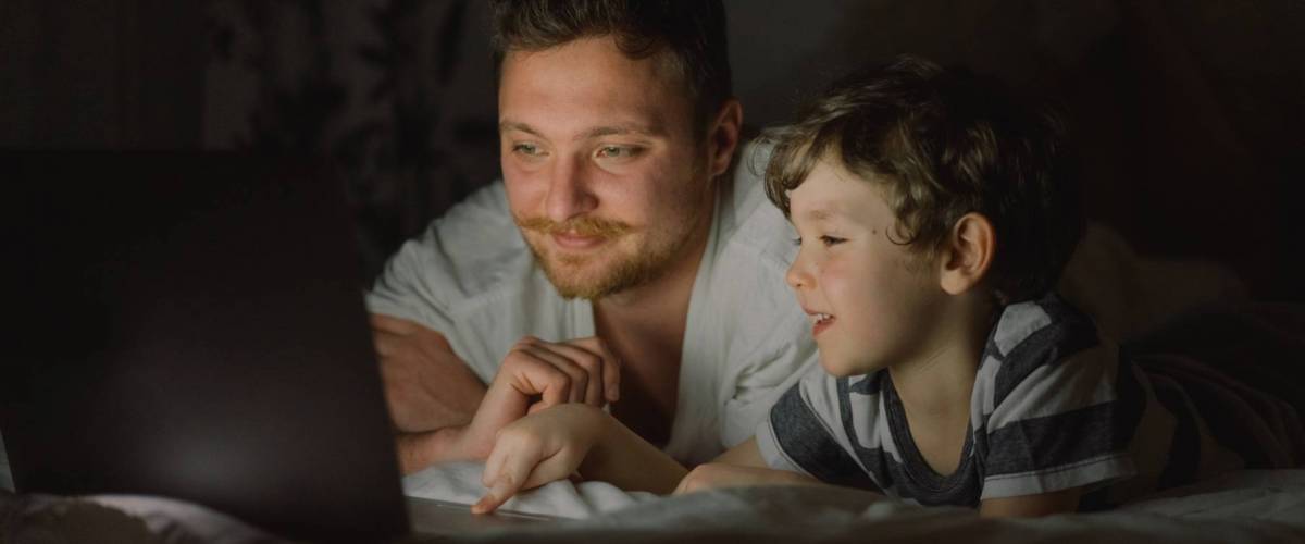 Father and son using laptop by night at home on the bedroom. Technology concept