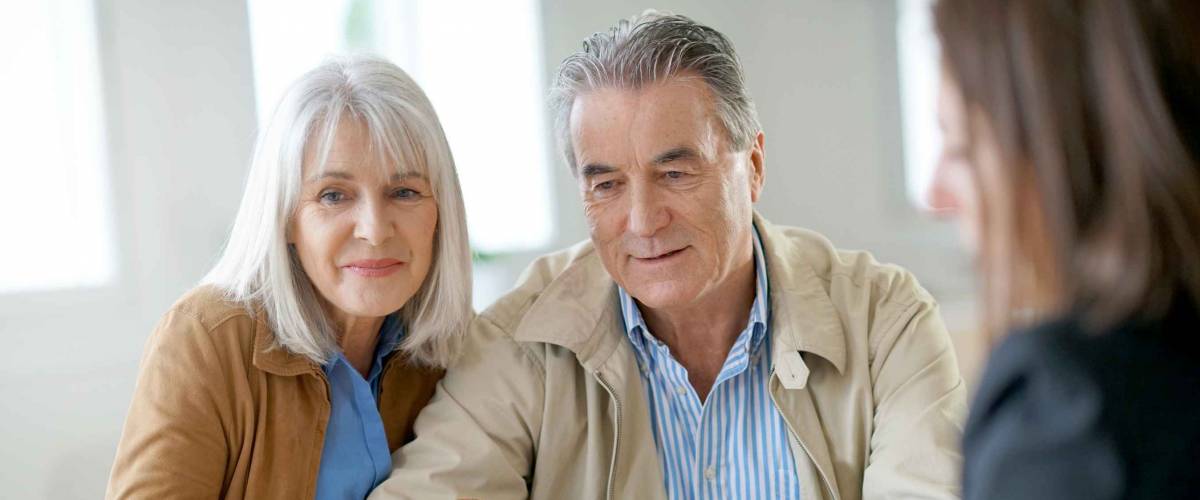 Senior couple meeting financial adviser as she shows them something on a piece of paper.