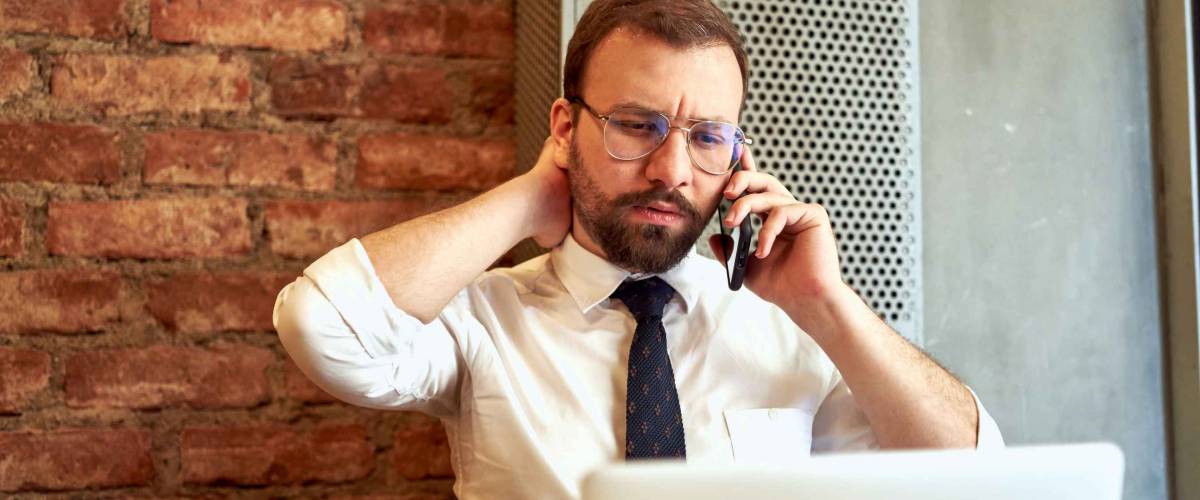 Man in white shirt and tie, stressed out on the phone.