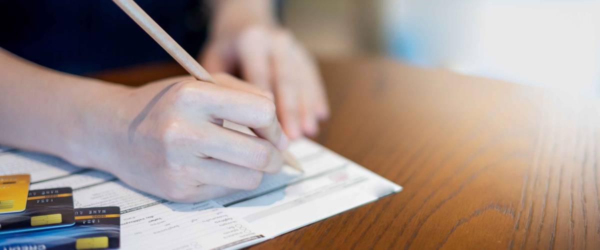 Close of up of woman writing with a pen on a piece of paper, credit cards beside her.