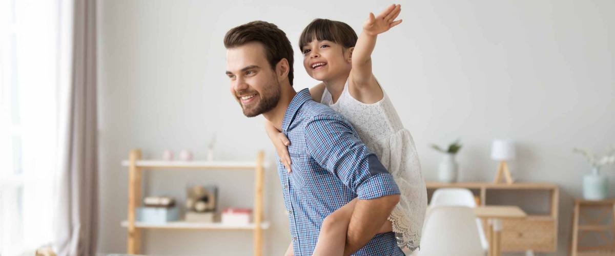 Happy dad piggybacking little funny daughter playing with daddy at home