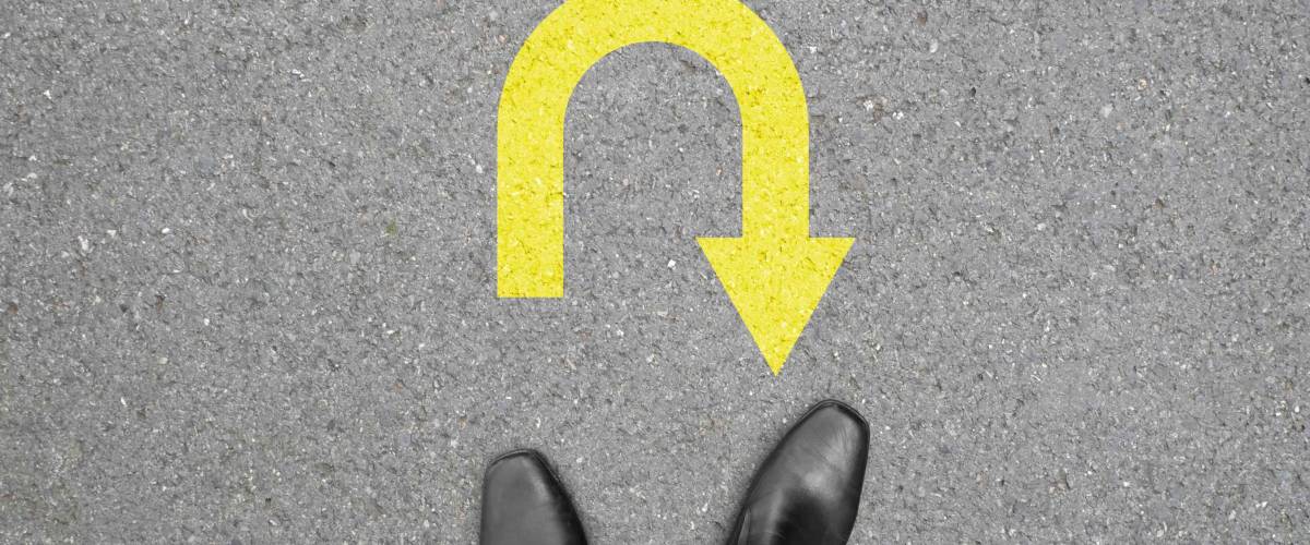 Businessman in black shoes standing at the u turn sign on the road. No way to go and have to turn back.