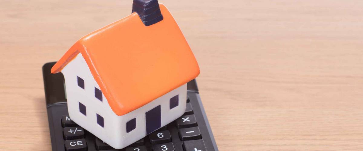 House miniature standing on calculator against wooden background