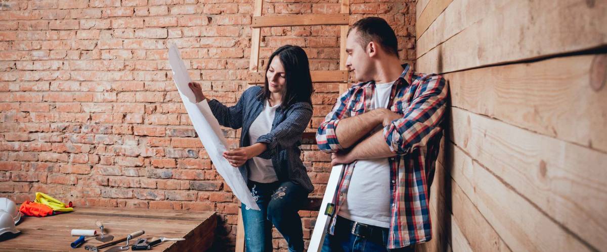Couple looking at blueprint for home in room under construction.