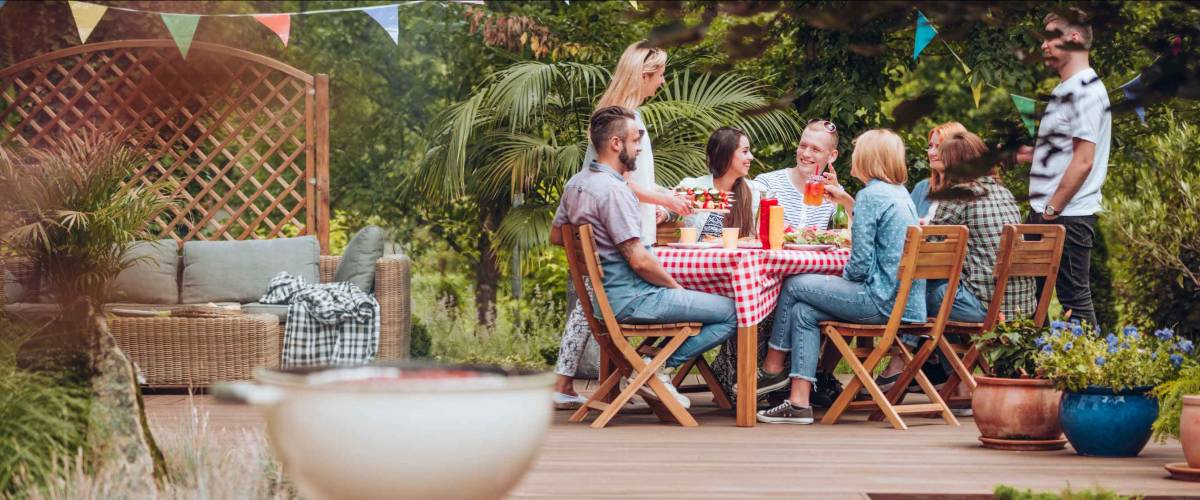 Group of people sitting in a backyard on a patio at a table, chatting.