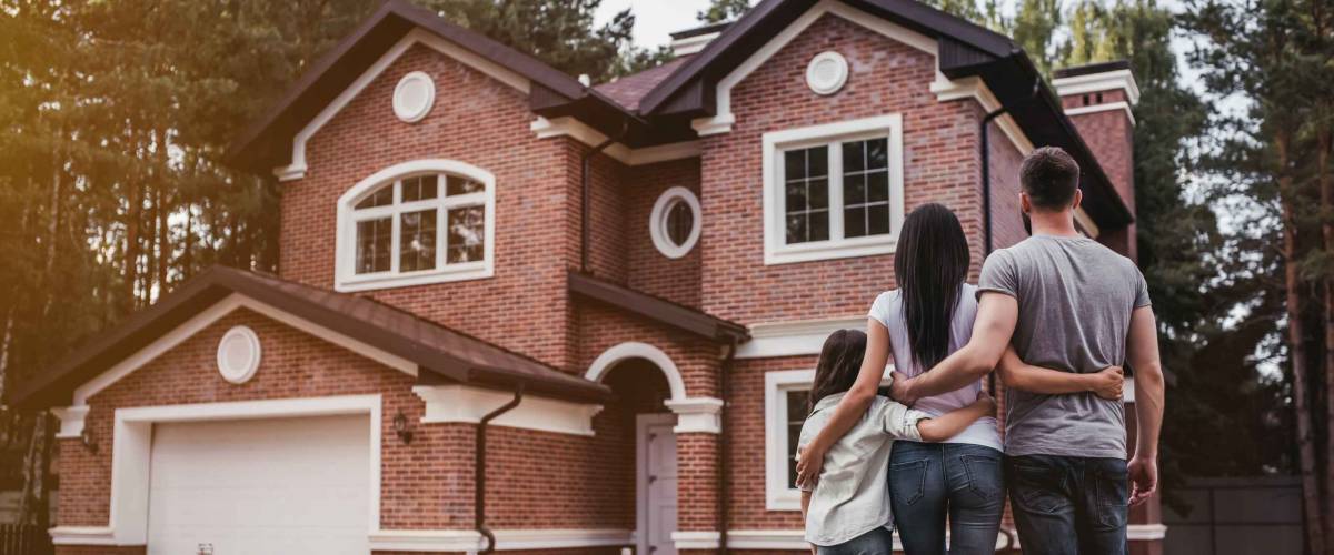 Back view of happy family is standing near their modern house and hugging