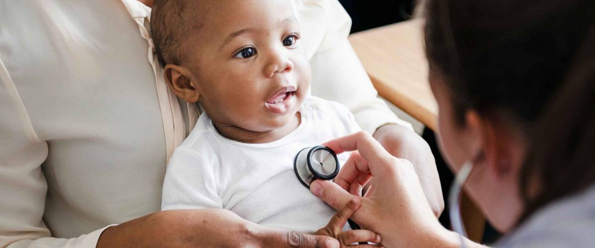 Doctor holds up a stethoscope to a baby's chest.