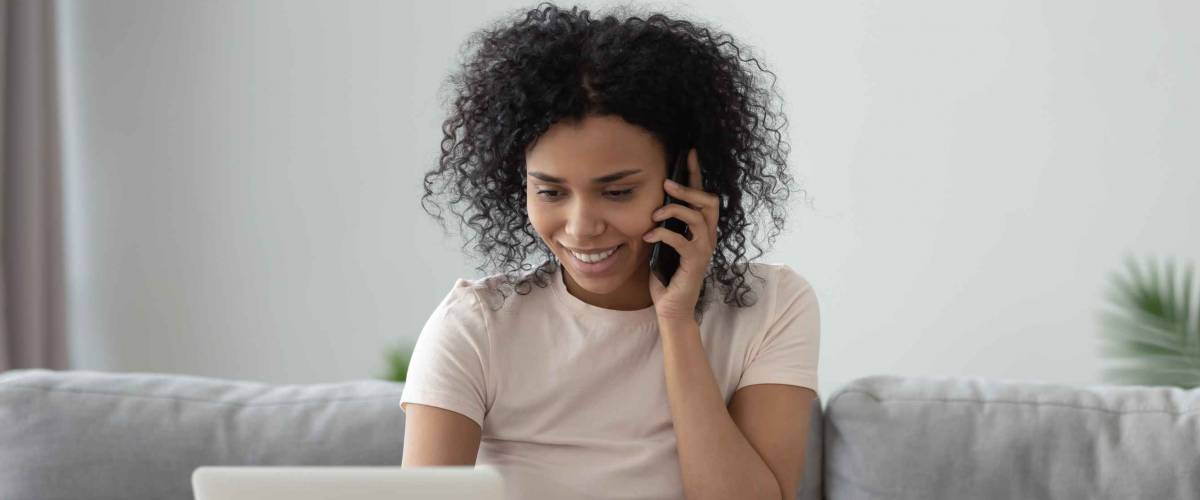 Woman sits on the couch on the the phone, looking down.
