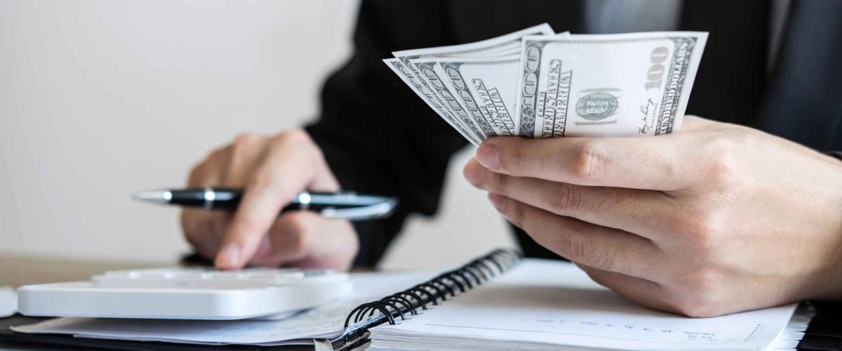 Close up of man's hands holding cash and using finger to type into calculator.