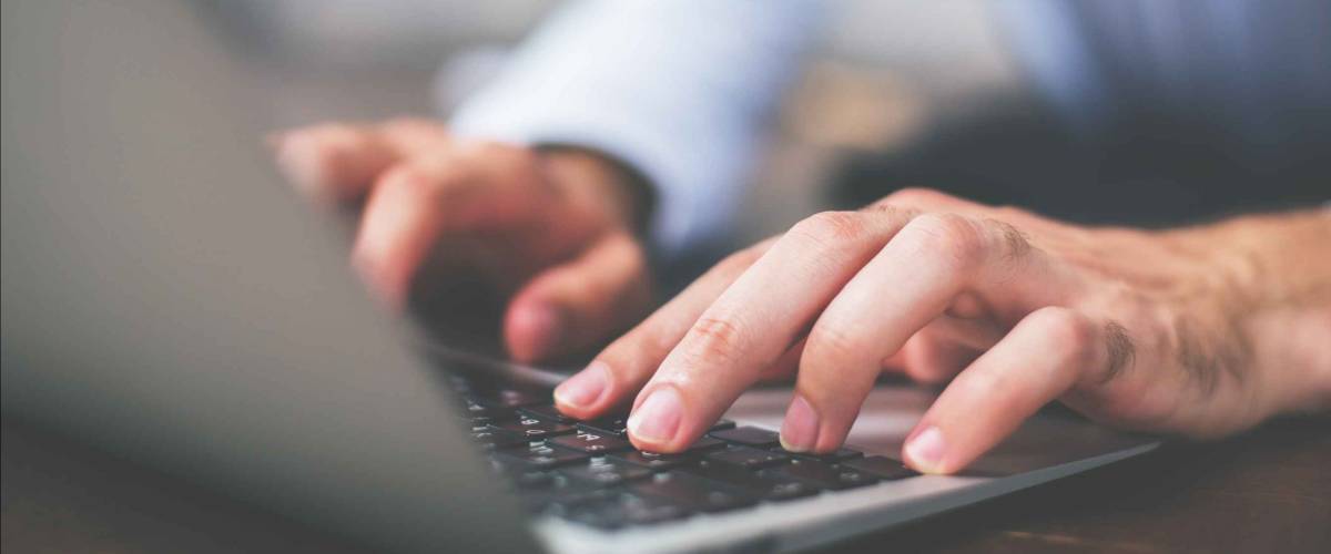Side view of male hands typing on laptop keyboard