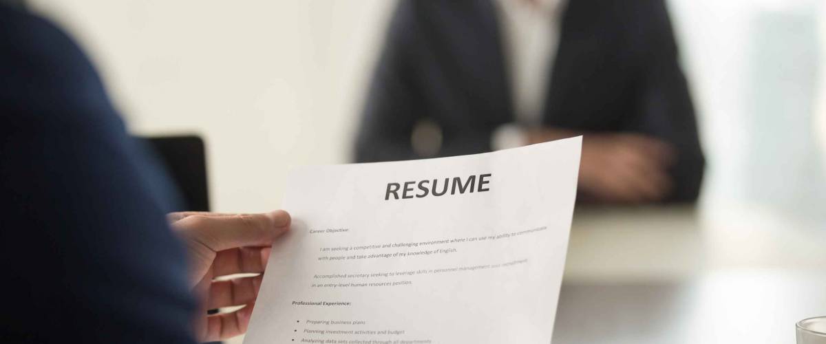 Close up view of job interview in office, focus on resume written at the top of a page.