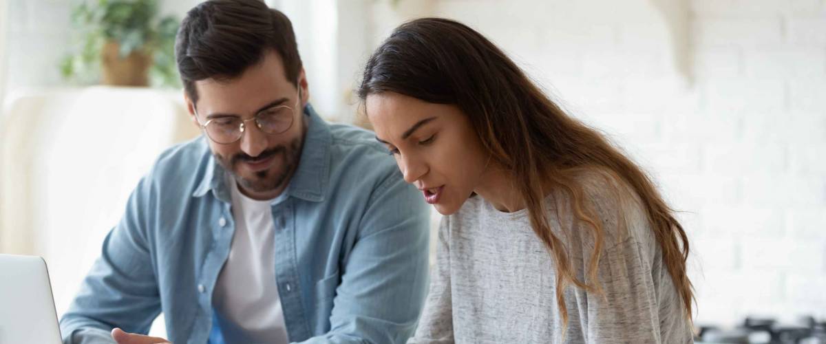 Young couple looking down at calculator while managing finances at kitchen table.