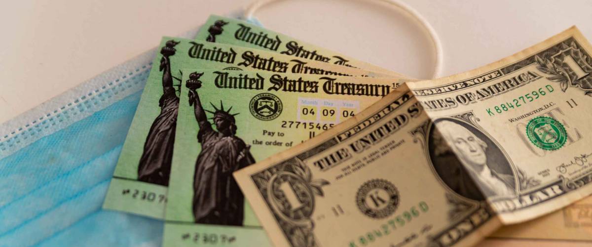 Washington, usa - 10 march 2021: close up of stimulus check and face mask and banknote on black background, concept of federal financial help given to stop economic crisis on white background