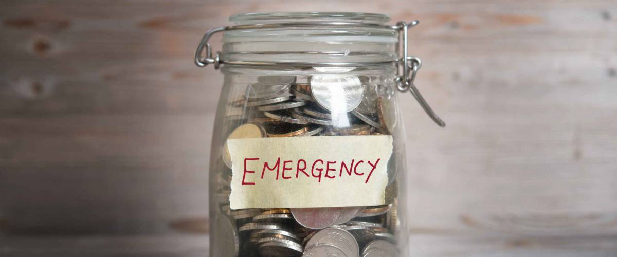 Coins in glass money jar with emergency label, financial concept. Vintage wooden background with dramatic light.