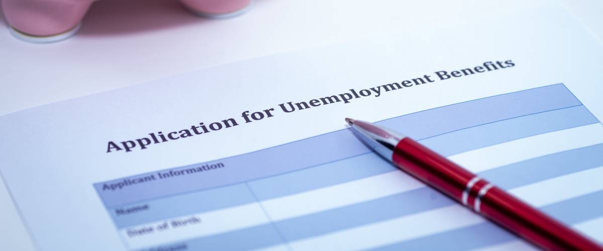 Piece of paper with Application for Unemployment Benefits typed on it, pen laying across it.