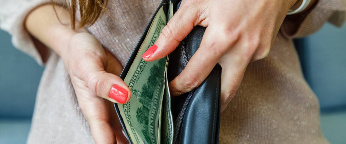 Woman opens wallet to sort through dollar bills.